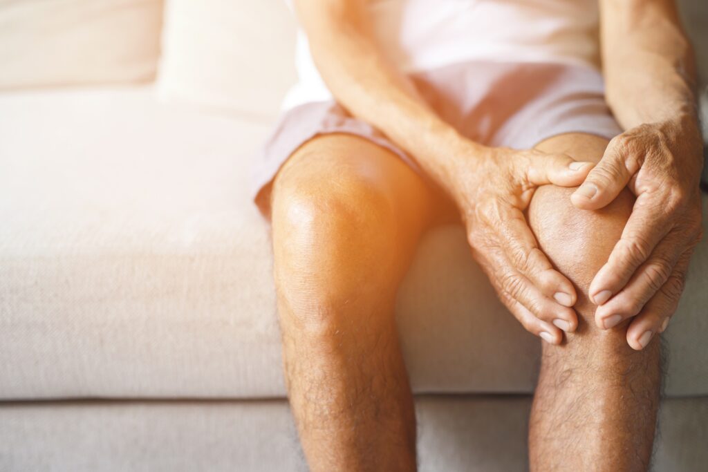 Man sitting on sofa holding knee from arthritis pain in Shelby Township, MI
