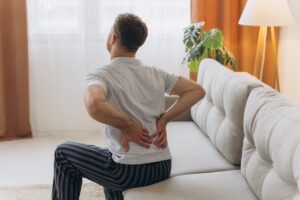 Man sitting on bed holding back due to chronic back pain in Shelby Township, MI