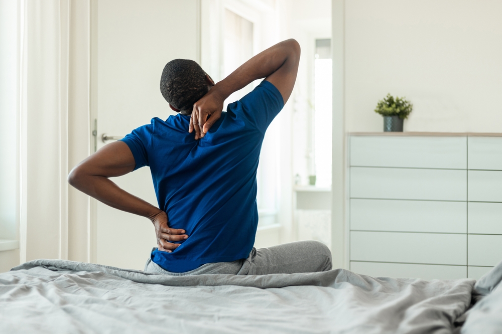 A man with back pain sitting on a bed holding his lower back